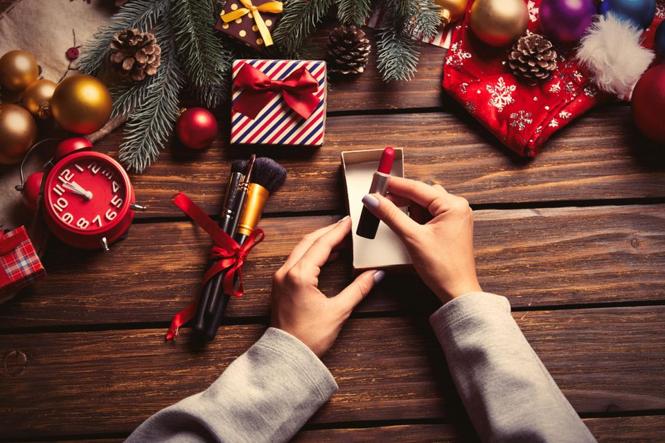 Beauty-Adventskalender, Frau nimmt Lippenstift aus kleiner Schachtel, kleine Geschenke um sie herum