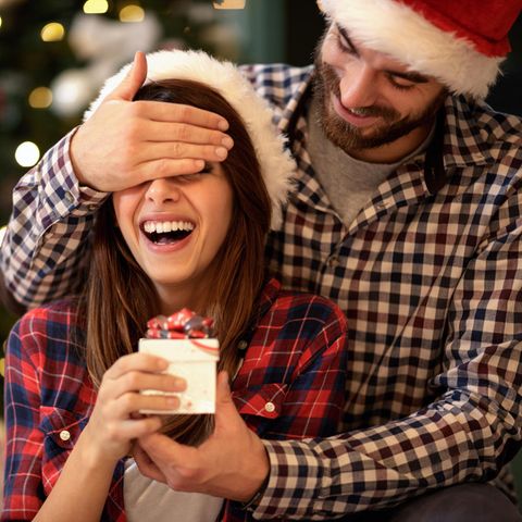 Adventskalender Paare, Frau bekommt kleines Geschenk von einem Mann überreicht, er hält ihre Augen zu