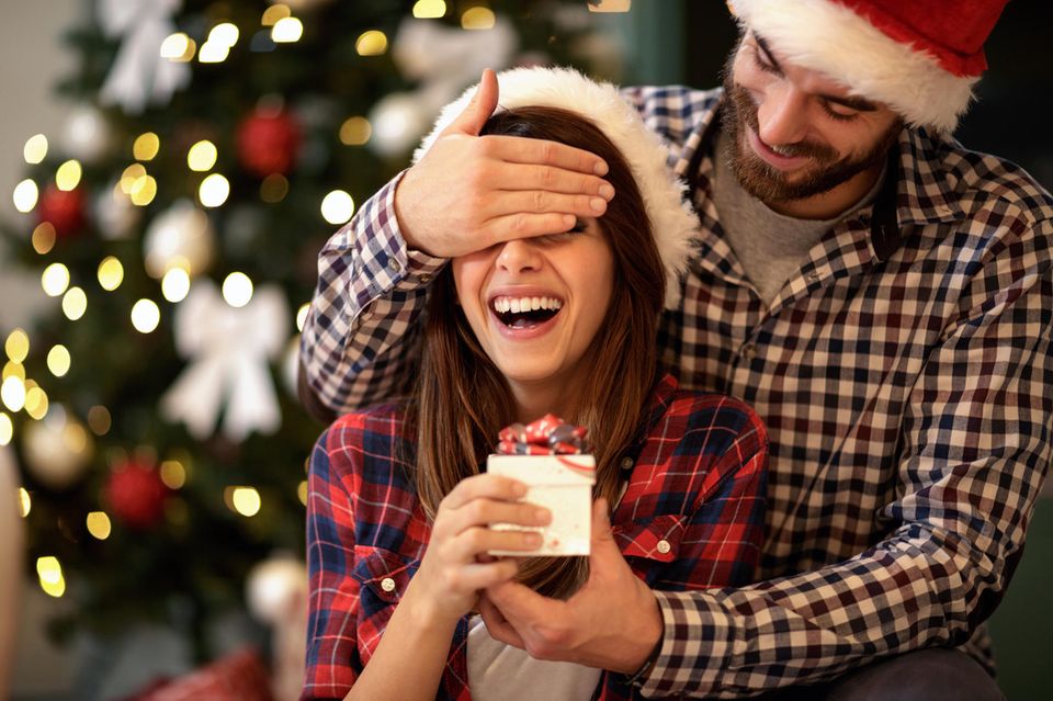 Adventskalender Paare, Frau bekommt kleines Geschenk von einem Mann überreicht, er hält ihre Augen zu