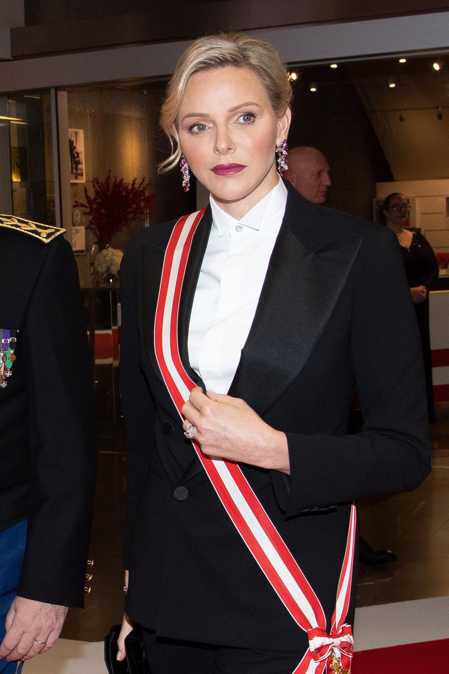 Während Fürstin Charlène am Nachmittag ganz in Weiß erschien, setzt sie abends auf eine schicke Zweiteiler-Kombination in Schwarz. Die rot gestreifte Schärpe ist ein toller Akzent auf der weißen, hochgeknöpften Bluse.
