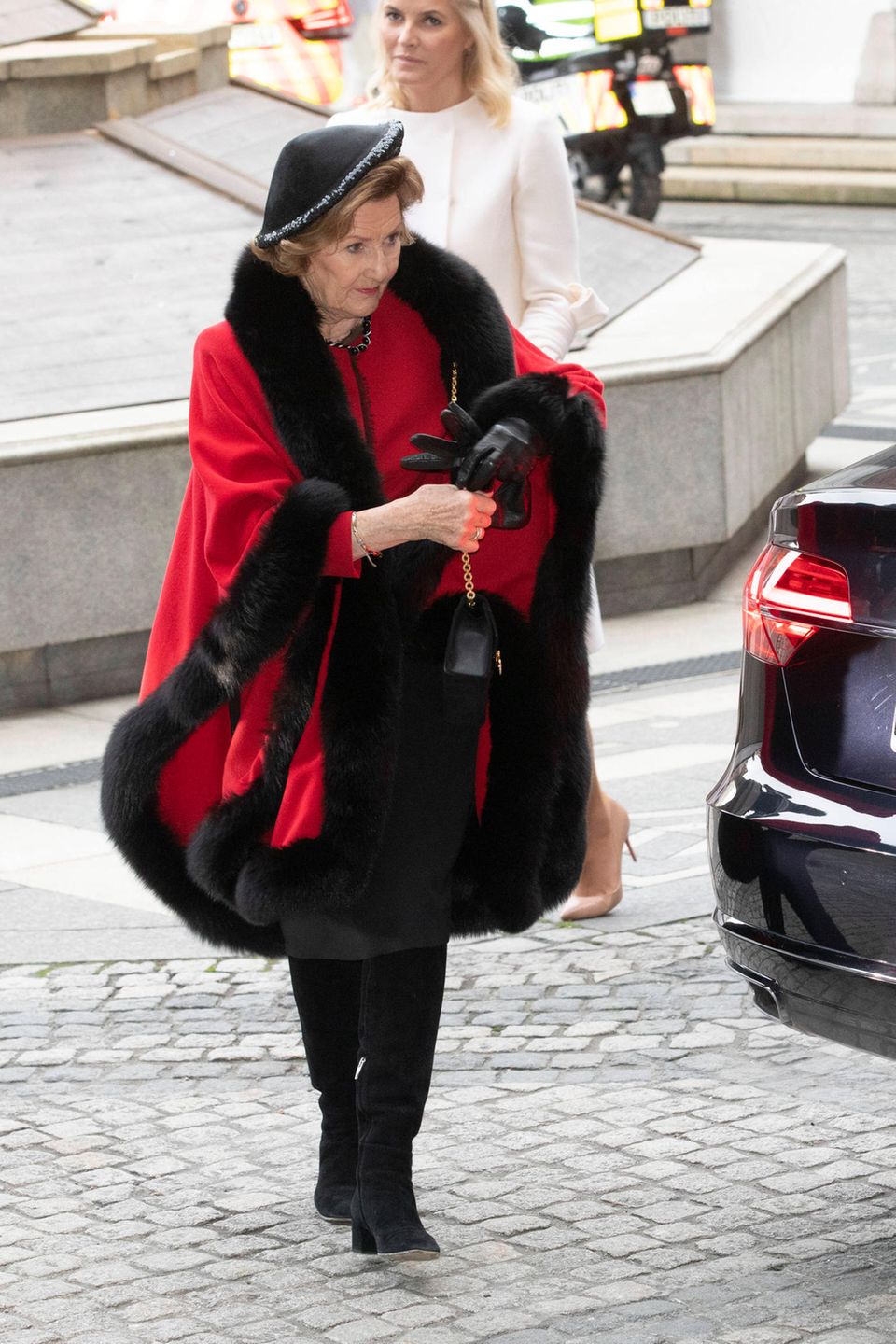 Königin Sonja trägt bei ihrer Ankunft im Rathaus von Oslo einen roten Mantel mit Pelzbesatz und Hut. 