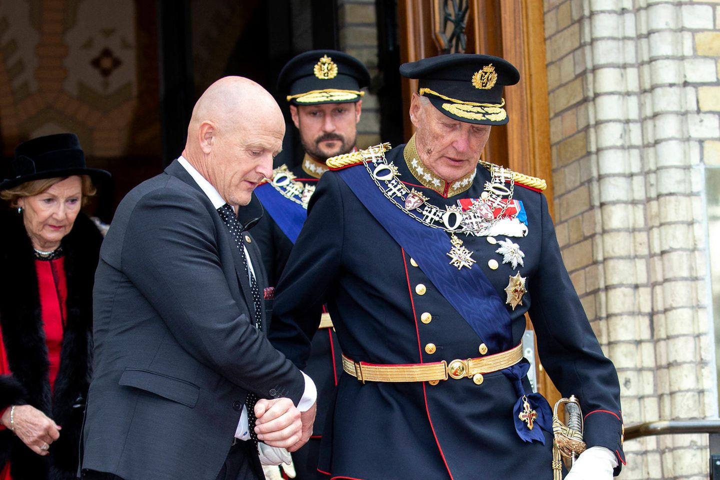 König Harald wird gestützt, hinter ihn gehen Königin Sonja und Prinz Haakon. Das Foto entstand im Oktober 2019.