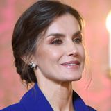 Mit Accessoires hält sich die schöne Monarchin zurück und trägt zum Tiefsitzenden-Chignon mit Steinen verzierte Perlenohrringe. Ihr Augen-Make-up ist mit den verstärkten Wimpern und dem rötlichen Lidschatten auffällig gehalten, während die Lippen ein dezenter Gloss zum Schimmern bringt. 
