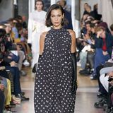 Was für eine Robe: Das französische Modelabel Lanvin zeigt auf dem Runway ein bodenlanges Kleid mit Raffungen am Hals und Volants am Saum. Bella Hadid präsentiert das Kleid außerdem mit langen schwarzen Handschuhen. 