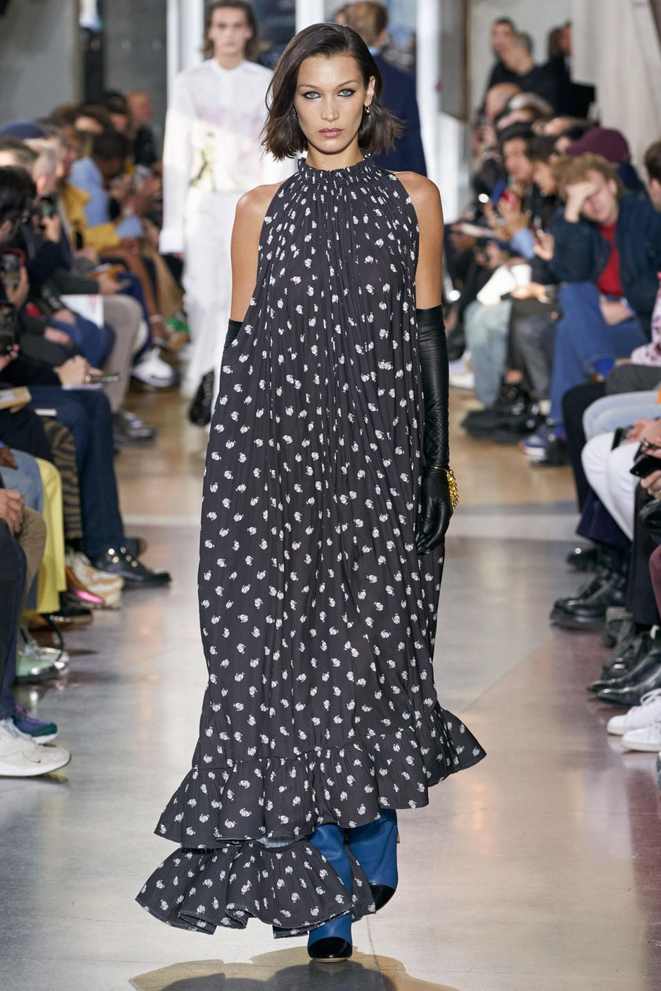 Was für eine Robe: Das französische Modelabel Lanvin zeigt auf dem Runway ein bodenlanges Kleid mit Raffungen am Hals und Volants am Saum. Bella Hadid präsentiert das Kleid außerdem mit langen schwarzen Handschuhen. Was für eine Robe: Das französische Modelabel Lanvin zeigt auf dem Runway ein bodenlanges Kleid mit Raffungen am Hals und Volants am Saum. Bella Hadid präsentiert das Kleid außerdem mit langen schwarzen Handschuhen.
