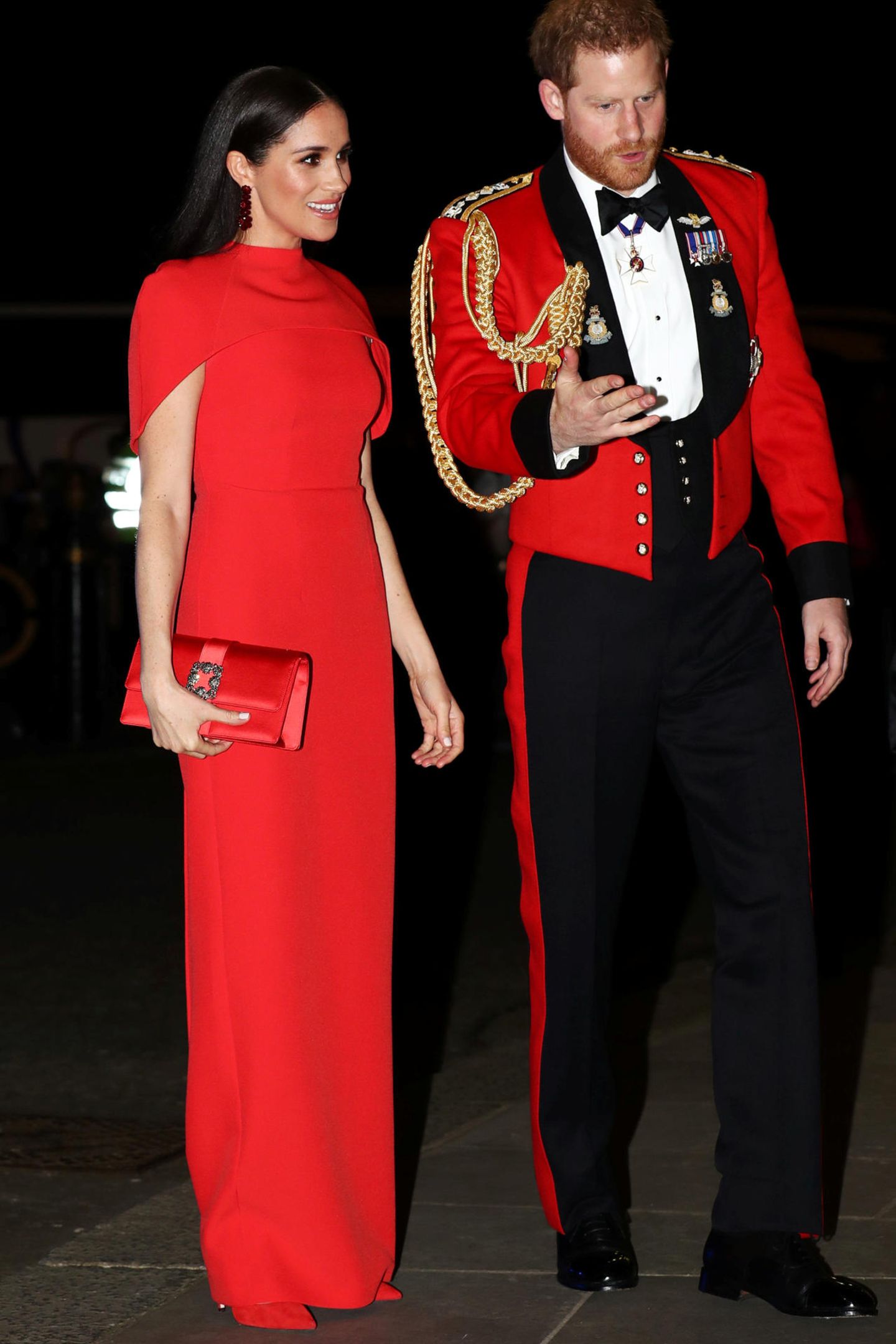 Die Herzogin von Sussex trägt eine bodenlange rote Robe im Stil eines Cape-Kleids von Safiyaa. Auch bei ihren Accessoires setzt Meghan auf Rot: So kombiniert sie Wildleder-Pumps von Aquazzura und eine Satin-Clutch von Manolo Blahnik zu ihrem Dress, die farblich allesamt perfekt aufeinander abgestimmt sind.