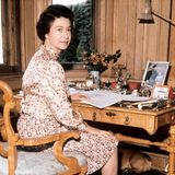 In ihrem königlichen Ferienhaus in Balmoral, Schottland, arbeitet Königin Elizabeth II. in einem mit Holz verkleideten Büro das den Blick auf die grüne Landschaft freigibt. Familienfotos und ein frischer Blumenstrauß zieren das karge Interieur.