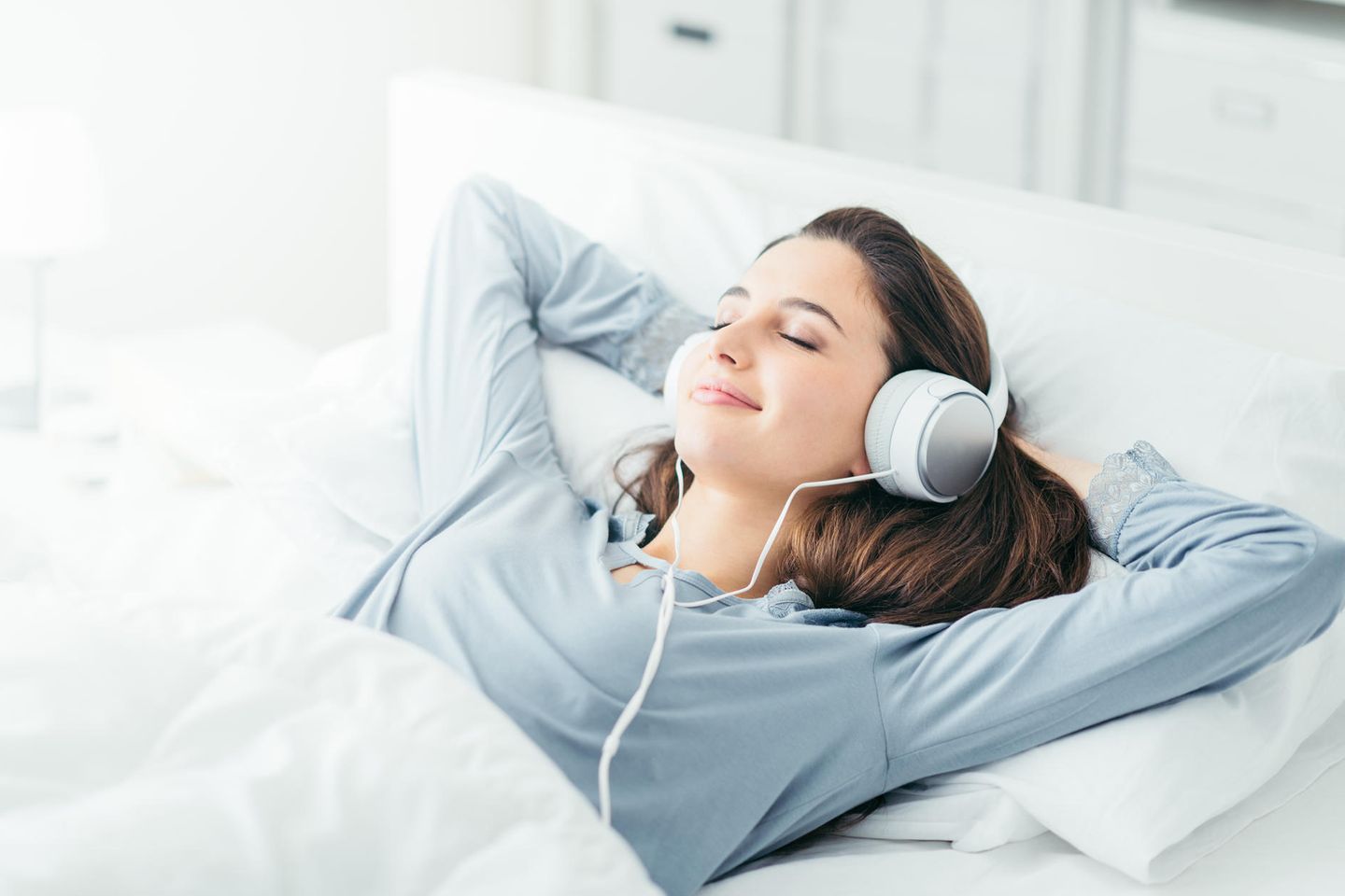 Frau liegt im Bett mit Kopfhörern