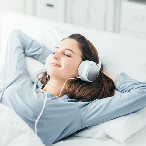 Frau liegt im Bett mit Kopfhörern