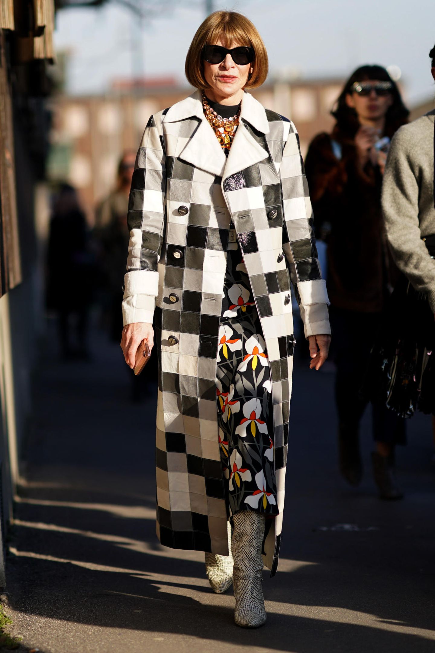 Bei der Fashion Week in Mailand macht Anna Wintour ihrem Namen als eine der einflussreichsten Frauen der Modebranche alle Ehre: Sie trägt ein Kleid mit Blumendruck, einen schwarz-weiß karierten langen Trenchcoat und stylishe Stiefel im Schlangendesign. Ihren glamourösen Look rundet sie mit einer Sonnenbrille und einer mit bunten Juwelen besetzten Statementkette ab.