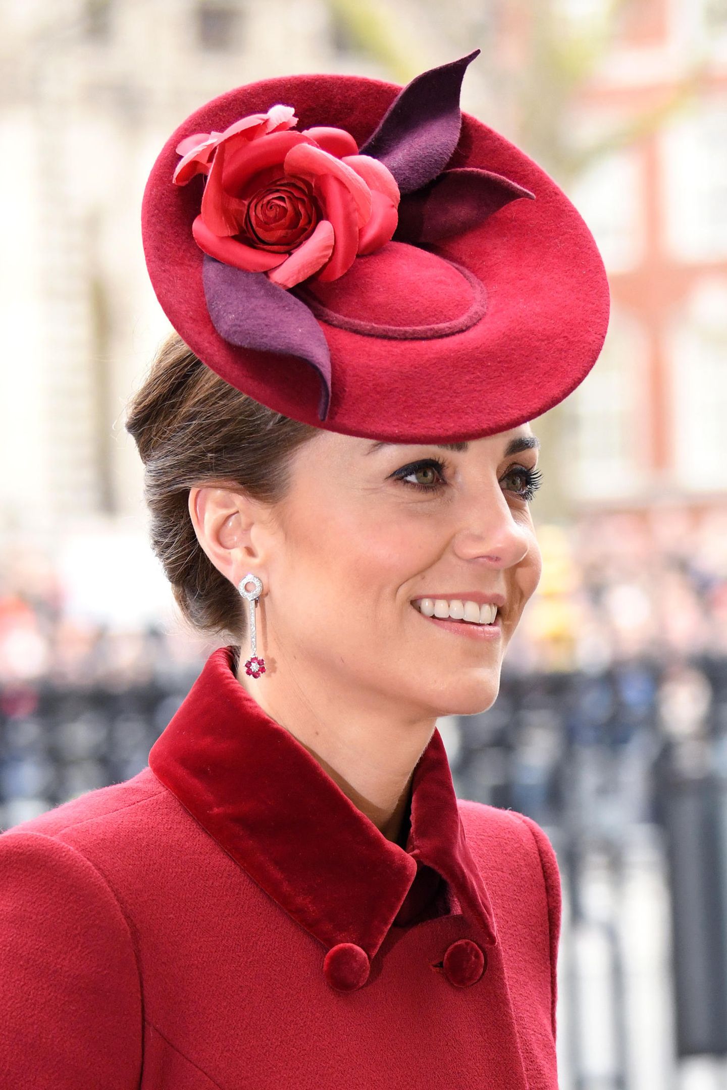 Auch Kate zeigt sich an diesem Tag mit dunkel betonten Augen und einem leichten Glow. Ihr brünettes Haar ist zu einem Dutt geknotet und lässt ihrer roten Kopfbedeckung mit floralen Applikationen so den großen Auftritt. 