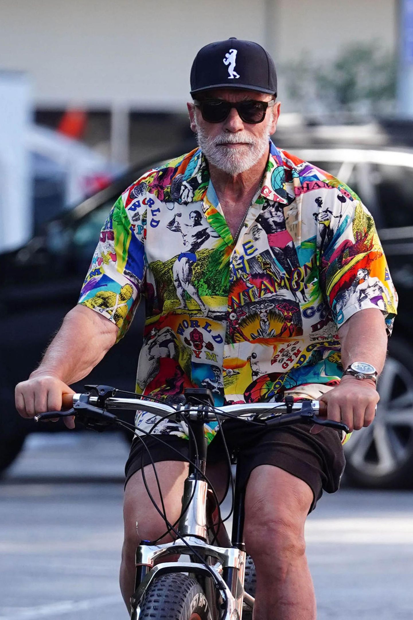 Rad-Fan Arnold Schwarzenegger dreht ganz regelmäßig seine Runden in L.A., doch so farbenfroh sieht man ihn selten. Nicht nur auf der Schirmmütze ist ein Bodybilder-Image zu sehen, das ganze Shirt ist mit bekannten Bodybuildern bedruckt. Auf seiner rechten Seite prangt ganz prominent ein schwarz-weiß Foto aus seiner eigenen aktiven Zeit.