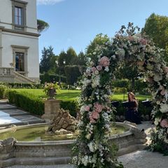 Wie aus einem Märchen! Die Hochzeit findet im Freien statt, vor einem Brunnen ist der Bogen aufgestellt, unter dem Sylvie Meis und Niclas Castello zum Ehepaar werden. Rosafarbene und weiße Blumen sind dort angesteckt. Im Hintergrund ist die Villa Cora, ein ehemaliger Adelssitz, am Ende des 19. Jahrhunderts gebaut, zu sehen. 