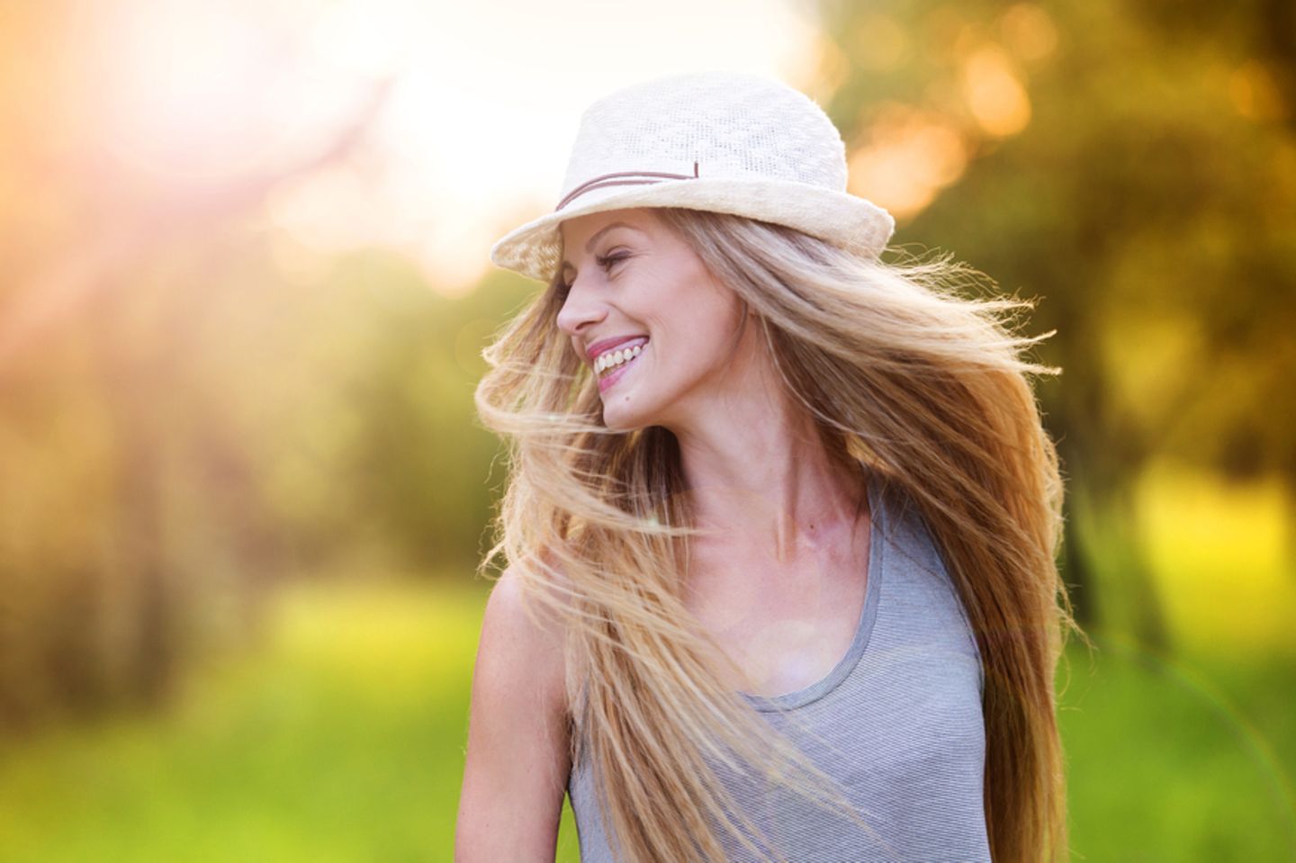 Dickere Haare bekommen: Lächelnde Frau mit langen blonden Haaren und Hut.