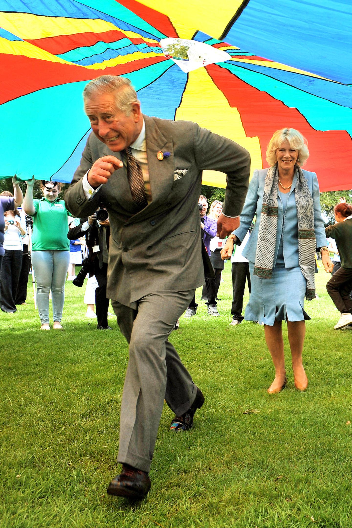 Da kommen Prinz Charles und Herzogin Camilla aber ins Schwitzen: Bei einem Besuch auf der britischen Kanalinsel Guernsey rennen die beiden unter einem riesigen Fallschirm durch.