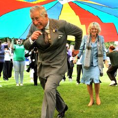Da kommen Prinz Charles und Herzogin Camilla aber ins Schwitzen: Bei einem Besuch auf der britischen Kanalinsel Guernsey rennen die beiden unter einem riesigen Fallschirm durch.