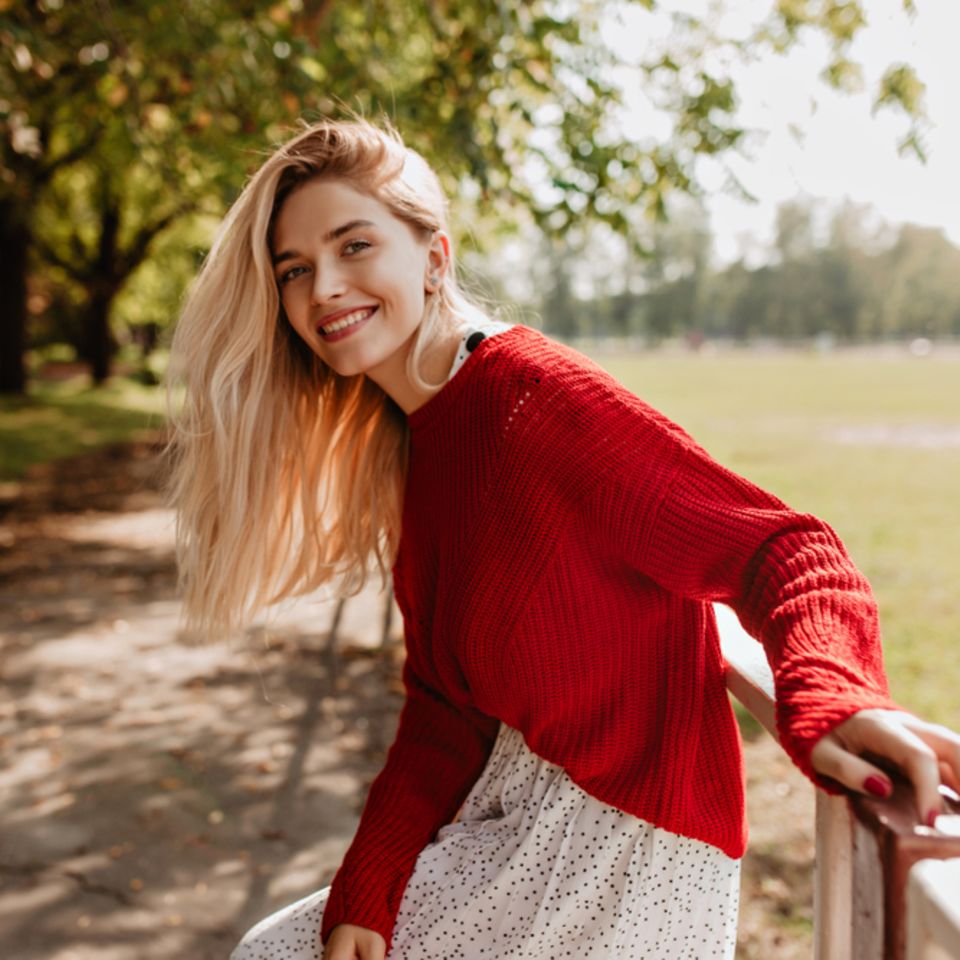 Resilienz stärken: Lächelnde blonde Frau mit rotem Pullover.