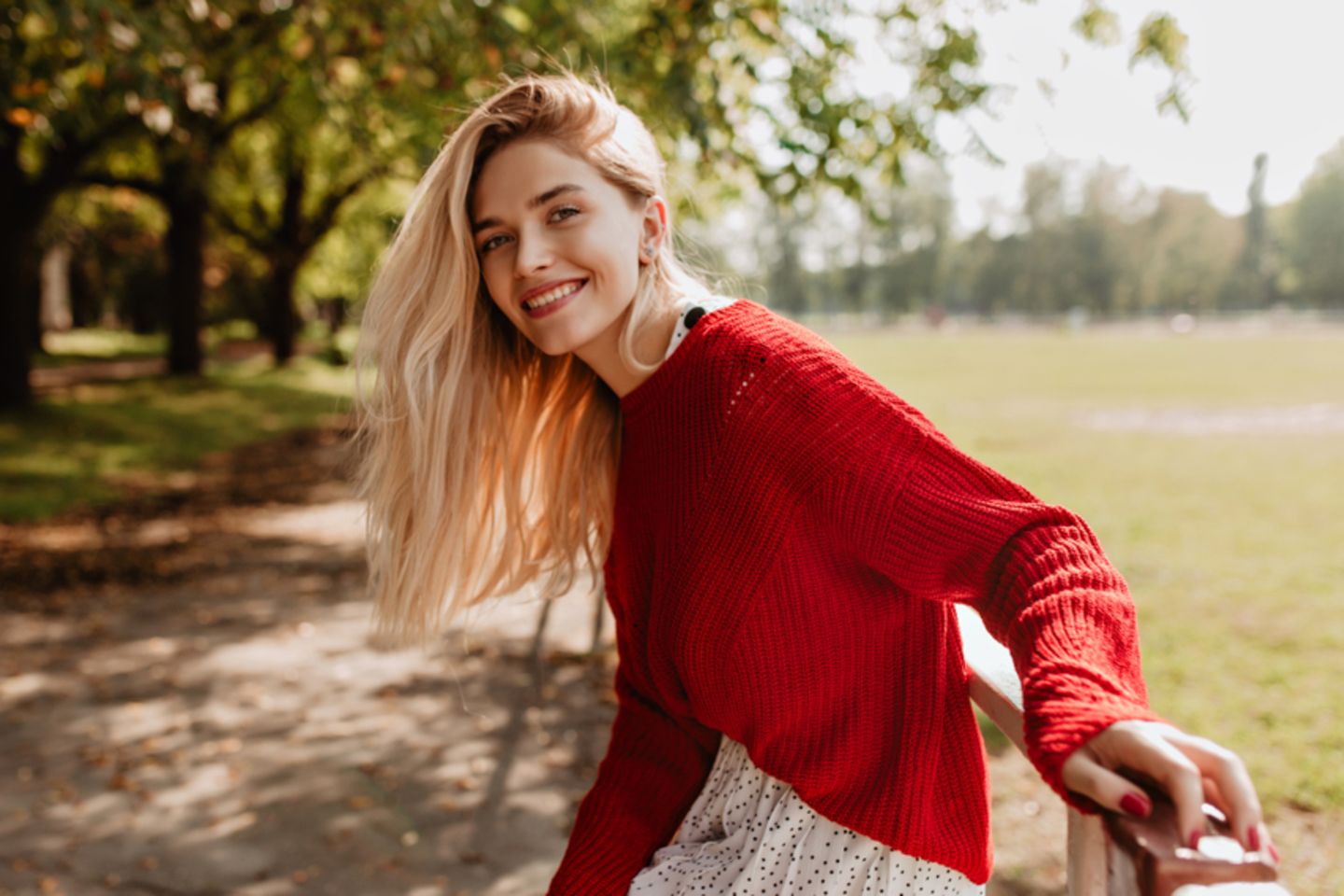 Resilienz stärken: Lächelnde blonde Frau mit rotem Pullover.