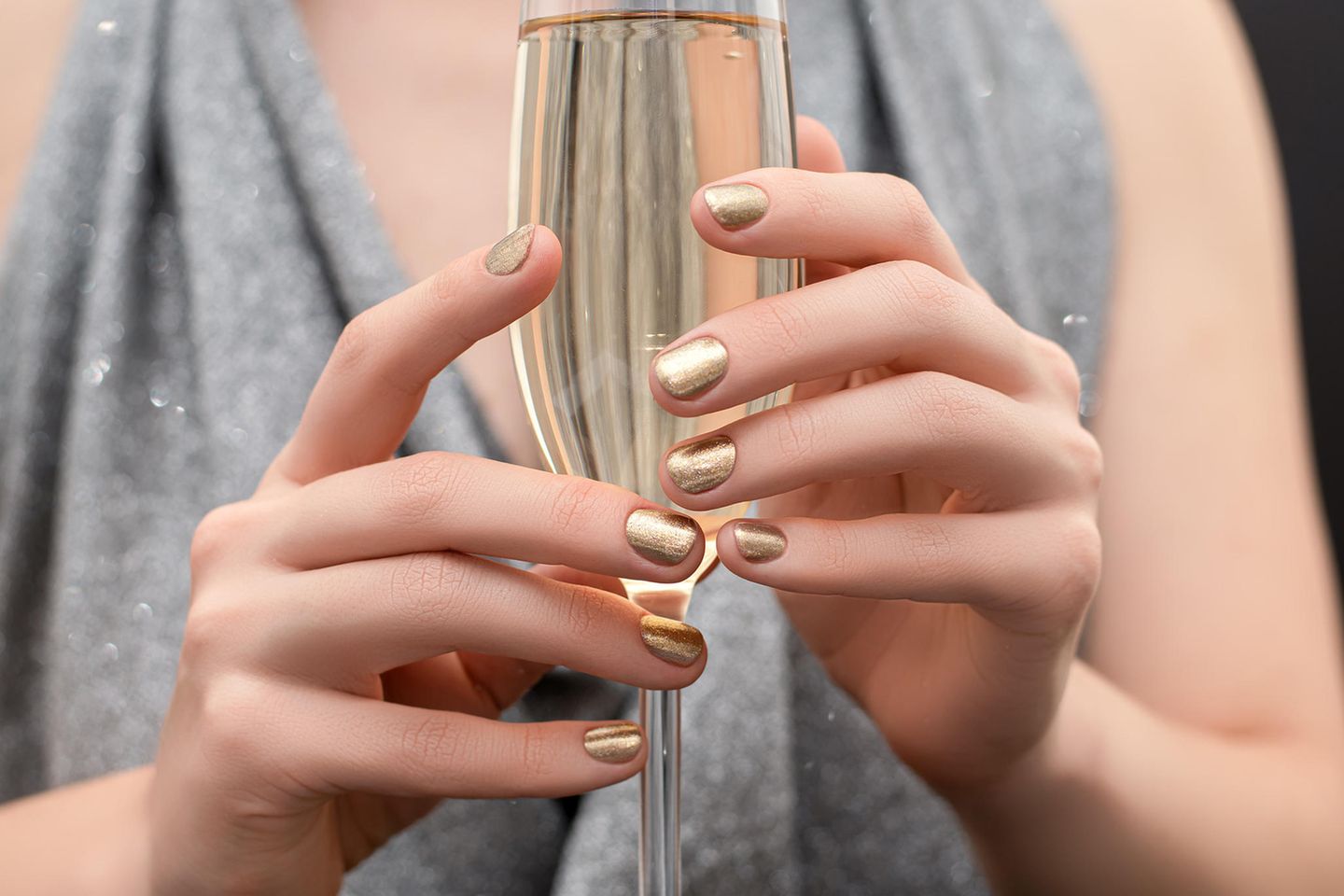 Silvester-Nägel: Frau mit goldenem Nagellack hält ein Glas Sekt in den Händen