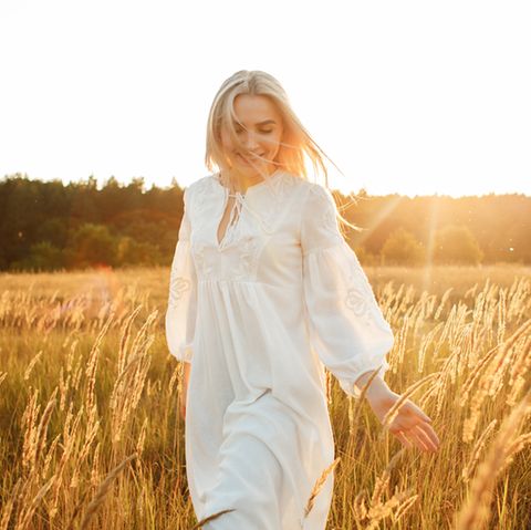 Aszendent Stier: Blonde Frau im weißen Kleid geht durch ein Weizenfeld.