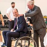 Nach mehreren verpatzten Würfen beim Rollstuhl-Basketballs im "Defence Medical Rehabilitation Centre Stanford Hall" schreitet Prinz Charles beherzt ein und schiebt seinen Sohn Prinz William näher an den Korb ran. Anschließend gibt es eine kleine Massage.