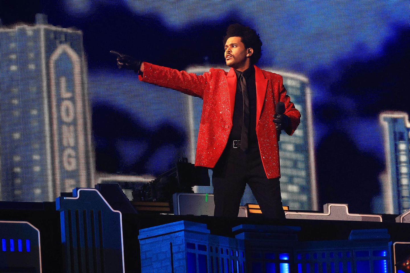 2021  In futuristisch-urbaner Kulisse performt The Weeknd beim diesjährigen Super Bowl mit lediglich 20.000 Zuschauern im Raymond James Stadium in Tampa, Florida. Sein Look ist mit knallrotem Pailletten-Blazer eher ein Look aus den Achtzigern.