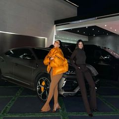 Kylie und Kendall lehnen lässig an einem Lamborghini Urus. Die orangefarbene Daunenjacke der jüngsten Schwester des Kardashian-Jenner-Clans ist perfekt auf den orangefarbenen Bremssattel abgestimmt. 
