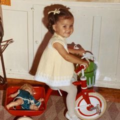 Kleine Zöpfchen, niedliches Kleid: Wer fährt hier ganz stolz Dreirad mit Puppe auf den Gepäckträger?
