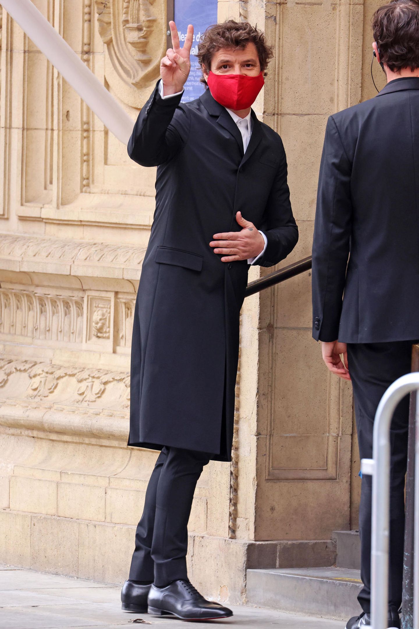 Schmale Hose, langer Mantel: Pedro Pascal weicht ein wenig vom klassischen Black-Tie-Look ab. Und um aufzufallen, hilft auch die rote Maske.