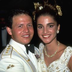 Zu den Feierlichkeiten am Abend wechselt das royale Brautpaar ihre Looks noch einmal: Prinz Abdullah trägt nun eine weiße Uniform, Rania tauscht ihren Schleier gegen floralen Schmuck im Haar und einen leichteren Bustier-Look mit den gleichen blumigen Applikationen.