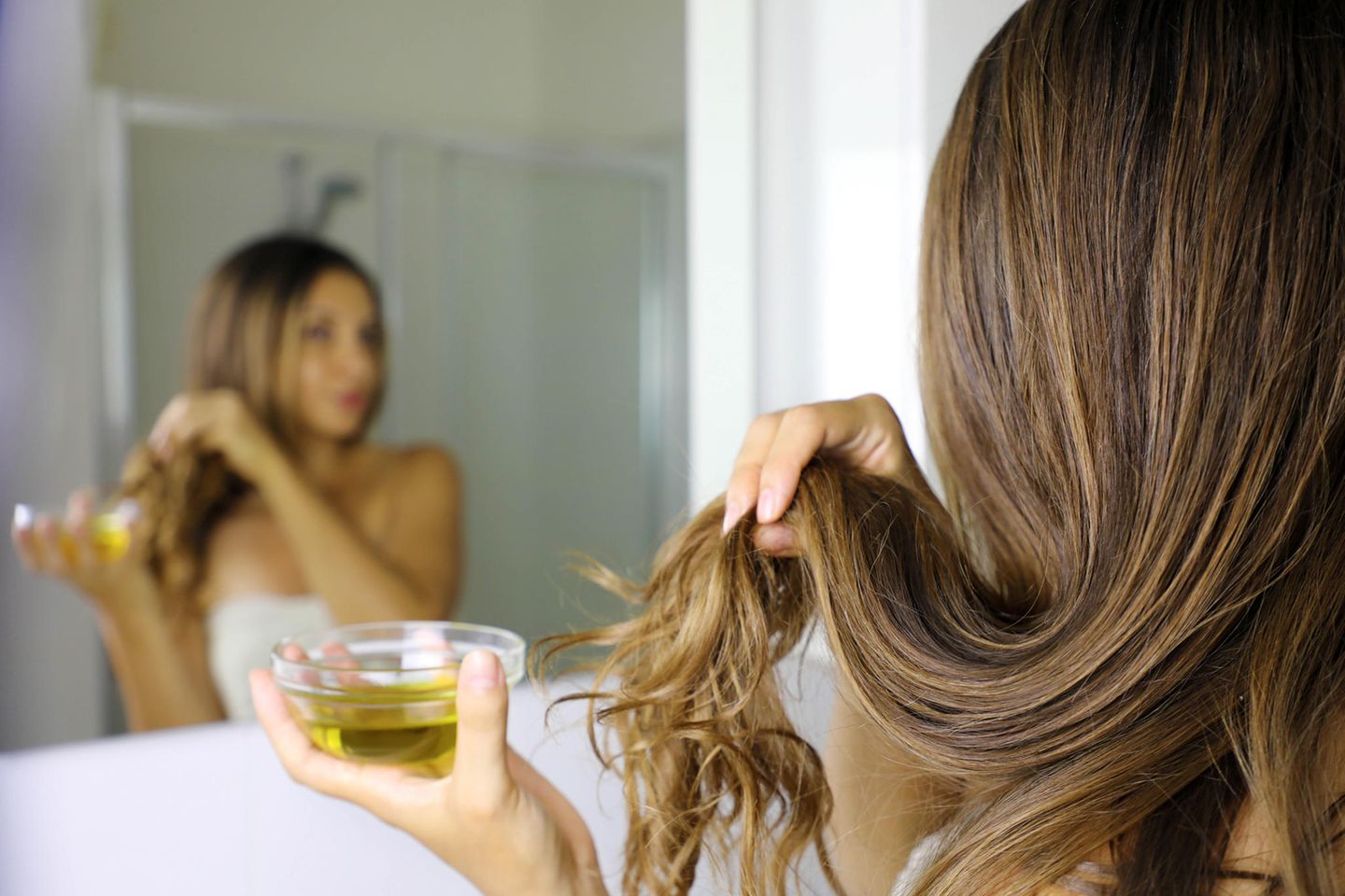 Rizinusöl, Frau vor einem Spiegel mit Haaren und Rizinusöl in der Hand