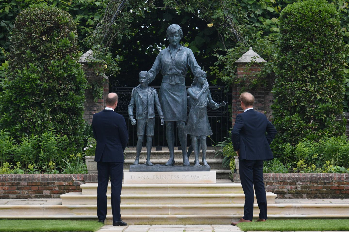 Prinz William und Prinz Harry betrachten das imposante Denkmal, das sie zu Ehren ihrer verstorbenen Mutter anfertigen haben lassen. Prinzessin Diana wird überraschenderweise nicht alleine abgebildet, sondern zusammen mit zwei Kindern, über die sie schützend ihre Hände hält - ein starkes Symbol für ihre Gutherzigkeit und ihr soziales Engagement.
