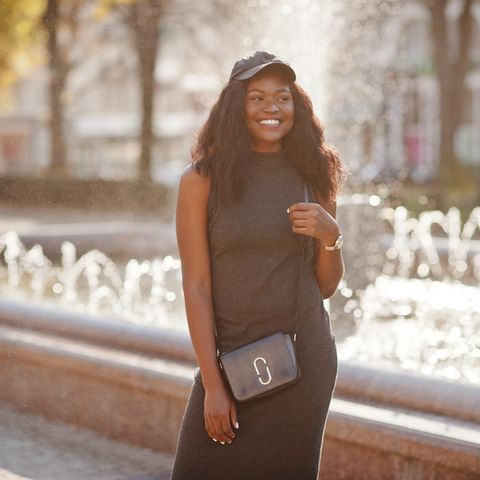 Crossbody-Tasche: Der Trend 2021, junge Frau vor Brunnen