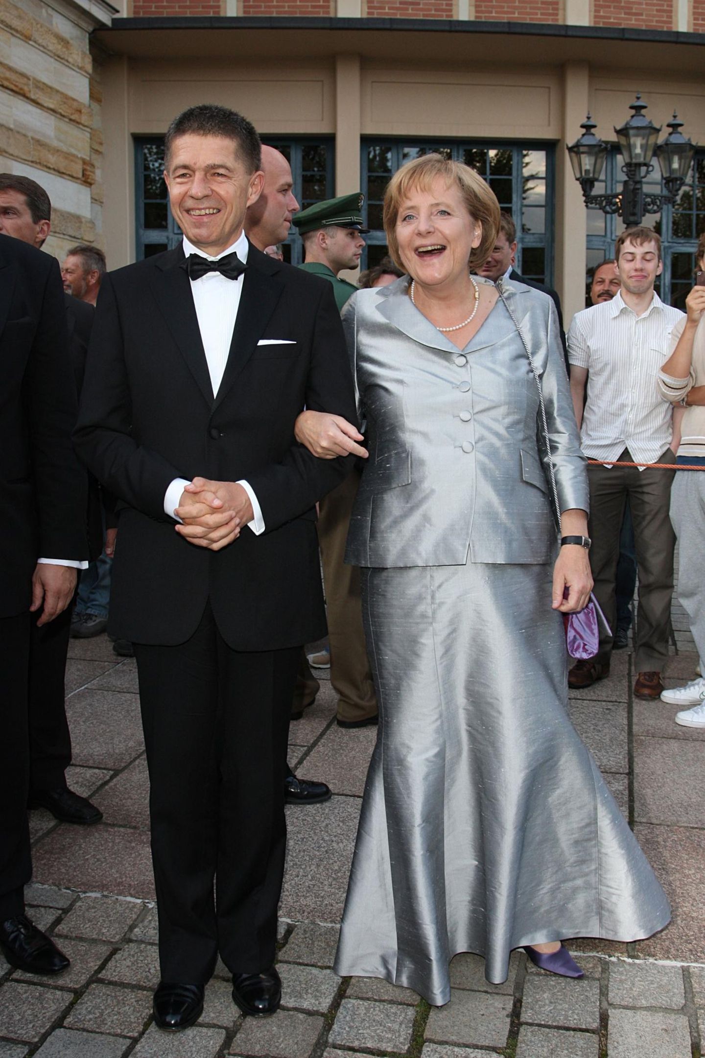 Joachim Sauer und Angela Merkel lachen in die Kamera.