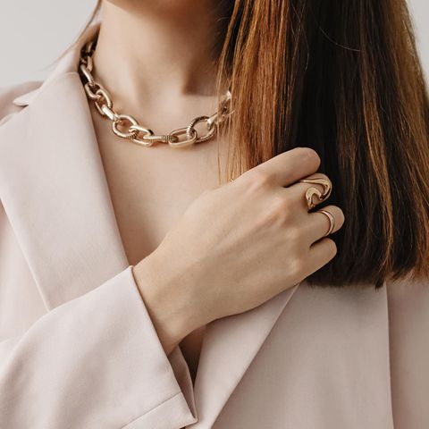 Eine Frau trägt eine goldene Statementkette sowie Ringe.