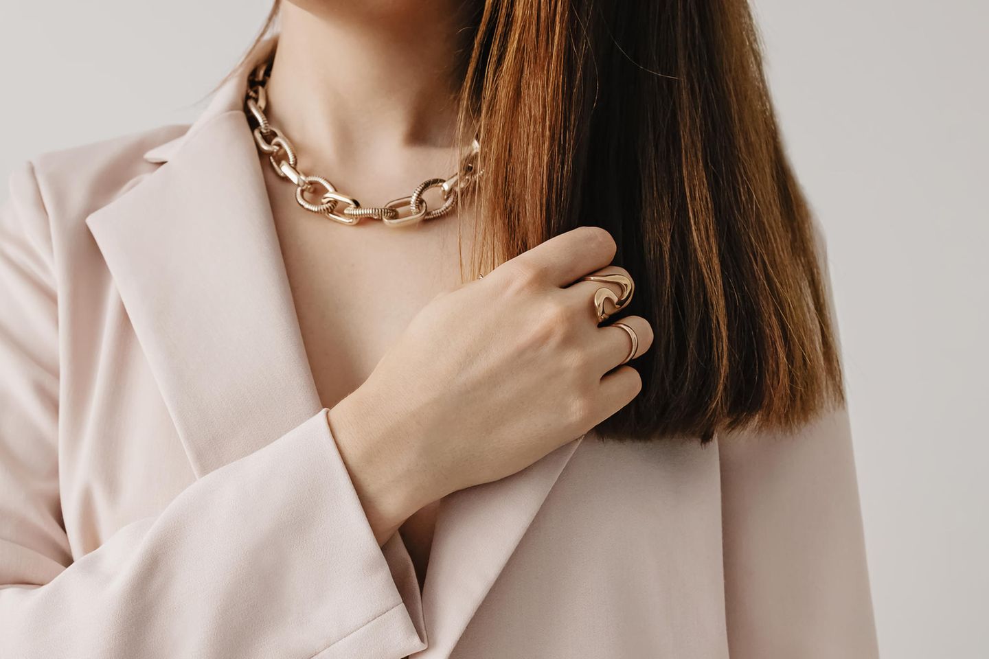 Eine Frau trägt eine goldene Statementkette sowie Ringe.