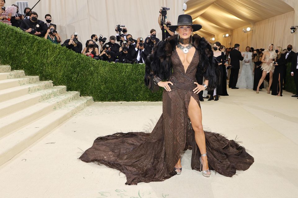 Howdy! Jennifer Lopez setzt auf ein Kleid mit Beinschlitz und XL-Ausschnitt von Ralph Lauren. Dazu kombiniert sie Hut, Felljacke und auffälligen Schmuck.
