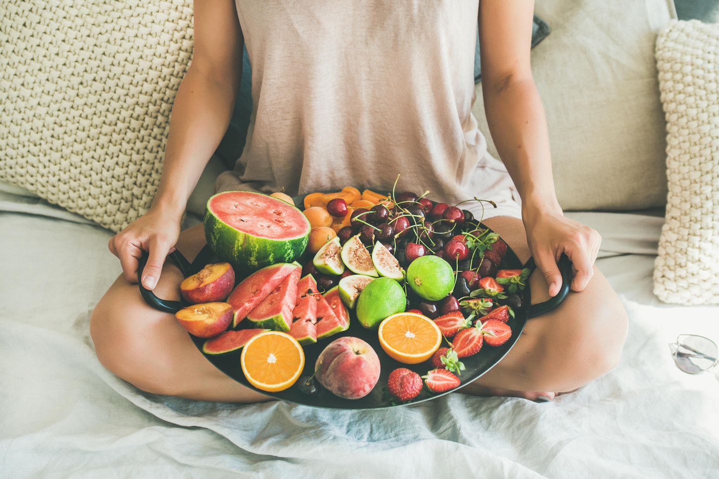 Frau hält einen Obstkorb mit Früchten wie Orangen, Wassermelone, Erdbeeren, Kirschen