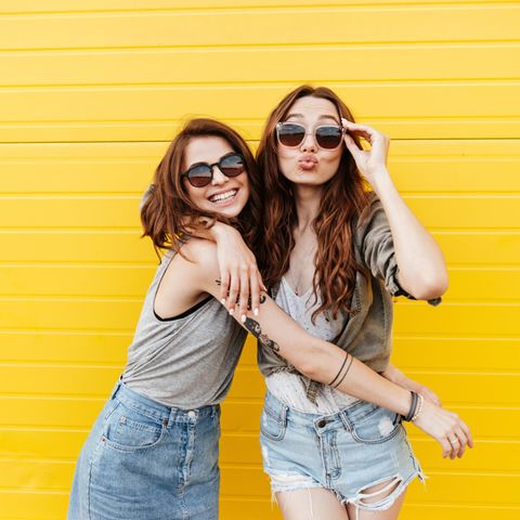 Farbpsychologie + Lieblingsfarbe: Zwei fröhliche Frauen stehen vor einer gelben Wand.