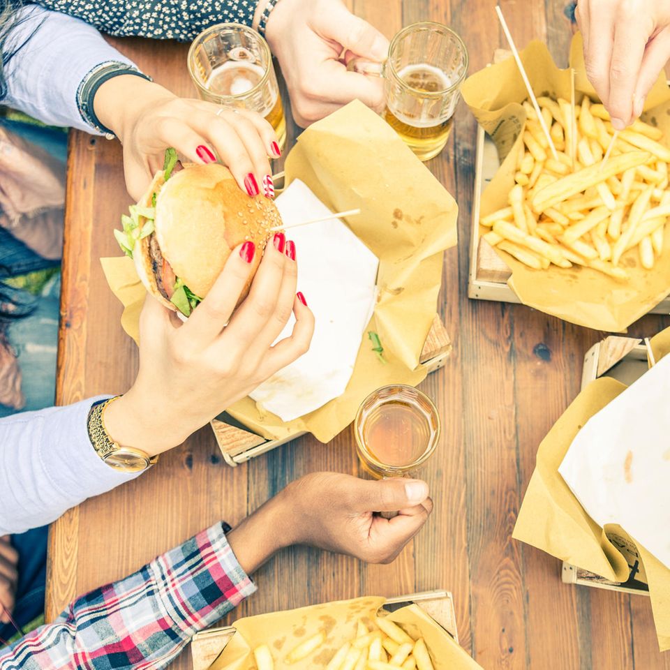 Entzündungsfördernde Lebensmittel: Menschen essen Burger mit Pommes und trinken Bier.