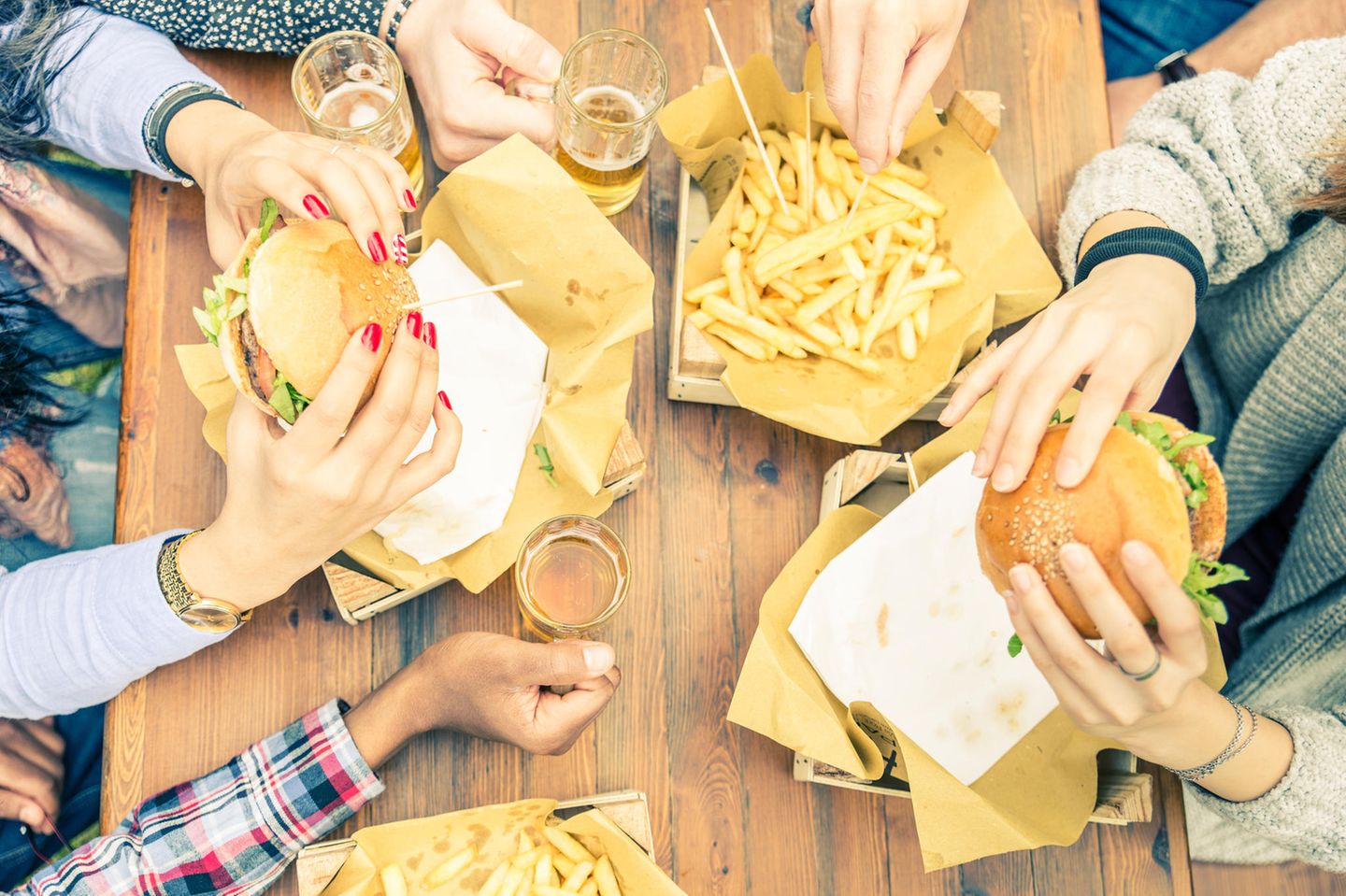 Entzündungsfördernde Lebensmittel: Menschen essen Burger mit Pommes und trinken Bier.