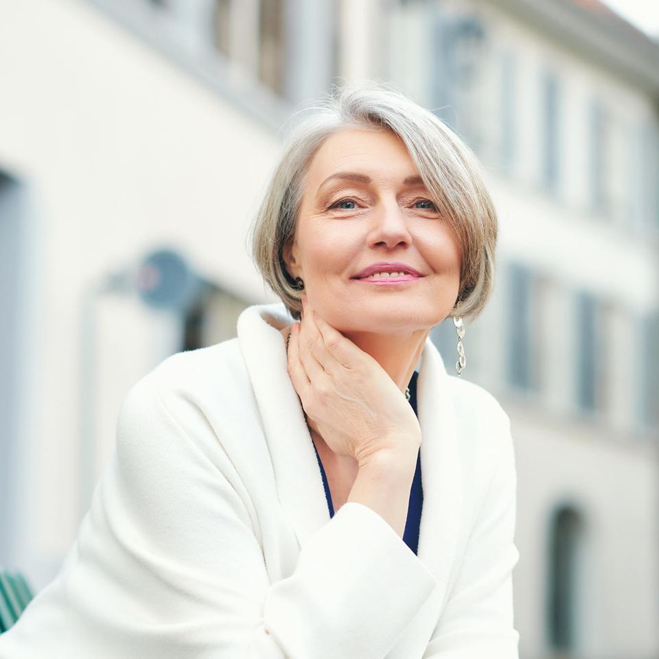 Frau über 50 sitzt auf einer Bank und lächelt