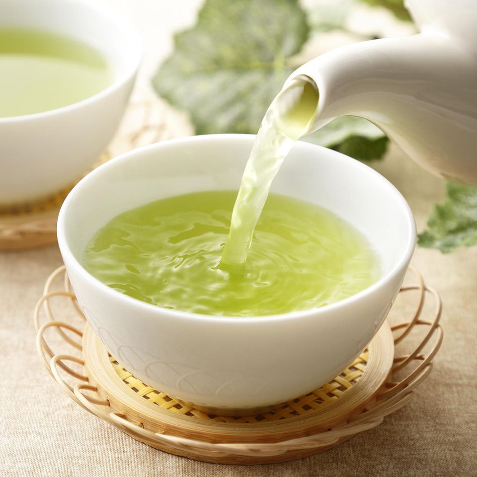 Grüner Tee wird in einen weißen Porzellanbecher eingegossen.