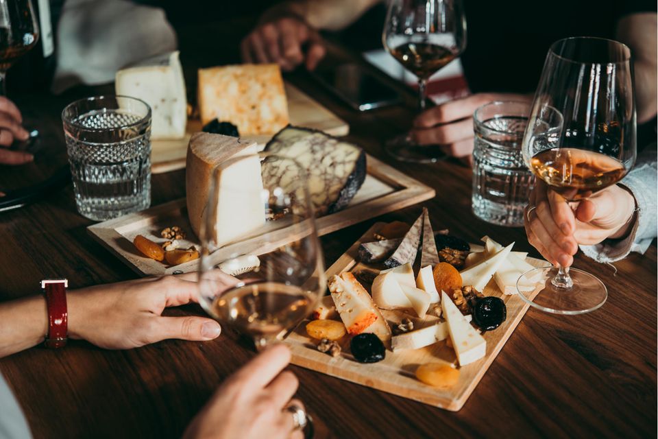 Zu viel Käse: Auf dem Tisch steht ein Brett mit verschiedenen Sorten Käse. Dazu gibt es Wein.