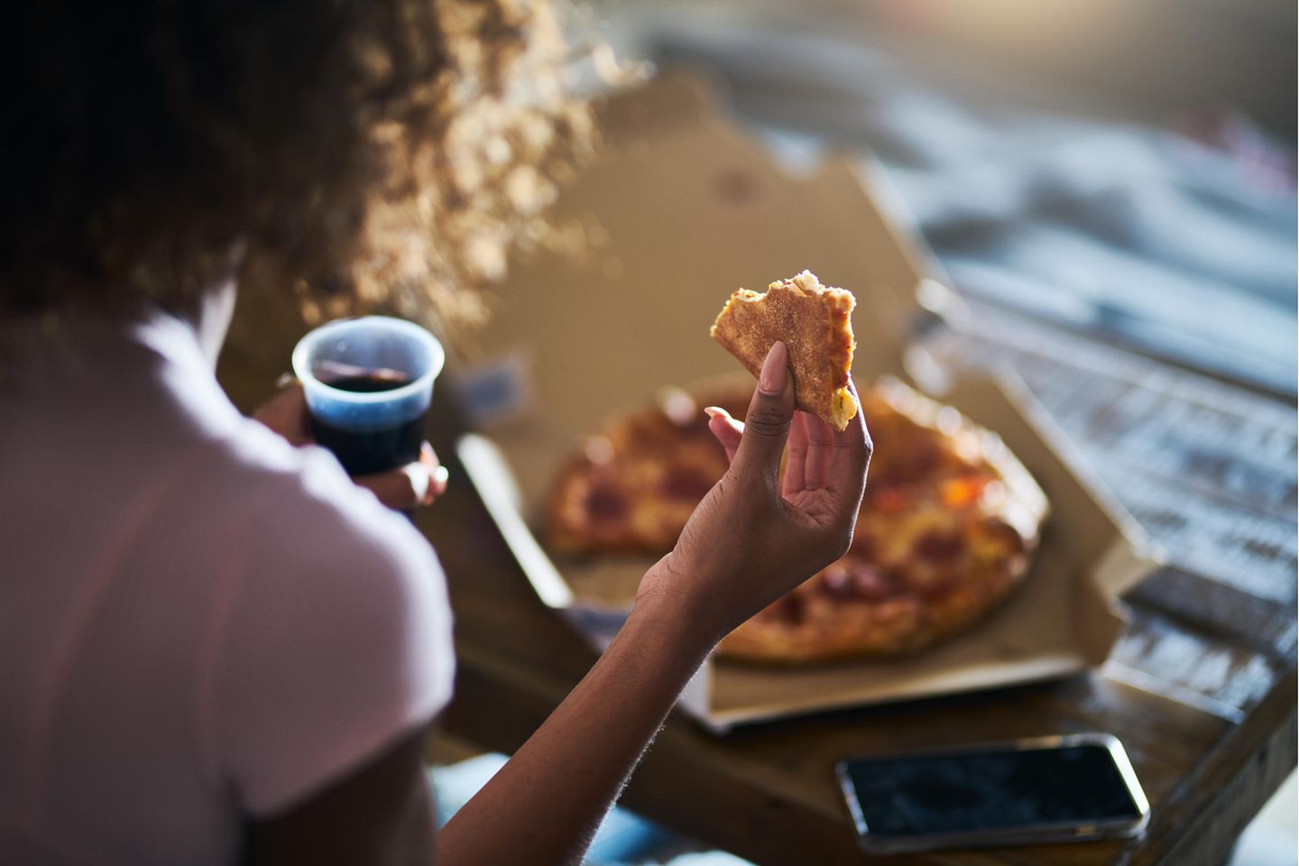 Wie Sie Ihre Pizza essen, verrät einiges über Ihre Persönlichkeit: Frau isst Pizza und trinkt Cola.