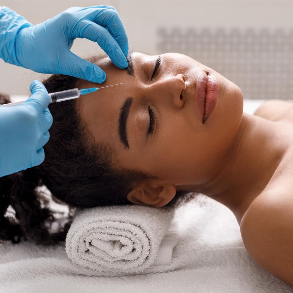 Ein Arzt injiziert einer Frau Botox zwischen den Augenbrauen