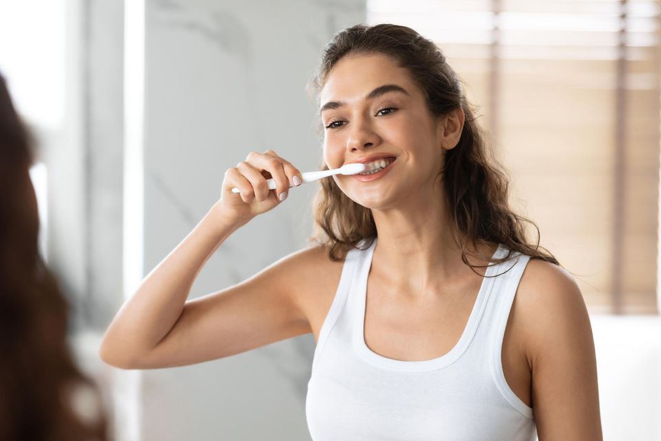 Frau putzt sich die Zähne vor dem Spiegel, Zahnpasta