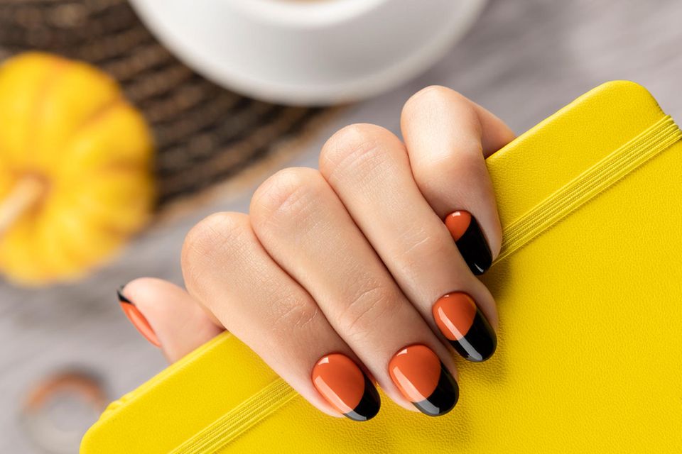 Halloween-Nägel 2021: Eine Hand mit orange-schwarz lackierten Nägeln