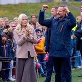 Im gemütlichen, pastellfarbenen 70er-Jahre-Look mit weitem Wollrock und Plateau-Stiefel hat Prinzessin Mette-Marit zusammen mit Prinz Haakon bei dem Besuch des Sportplatzes in Bergtunet Våler ihren Spaß.