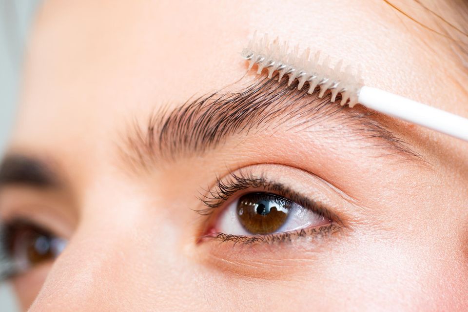 Augenbrauengel: Schöne Frau mit Augenbrauen, die Augenbrauengel mit einer Augenbrauenbürste aufträgt